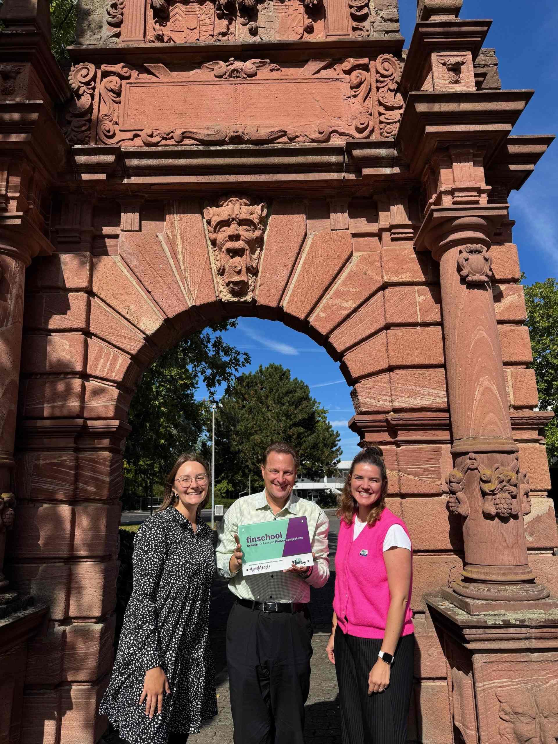 Foto: Marie Langeloh (links) und Jana Titov von der finlit Foundation überreichten HOLA-Fachbereichsleiter Stefan Prochnow die Auszeichnung als finschool (Foto: Swantje Stein-Hellmann).