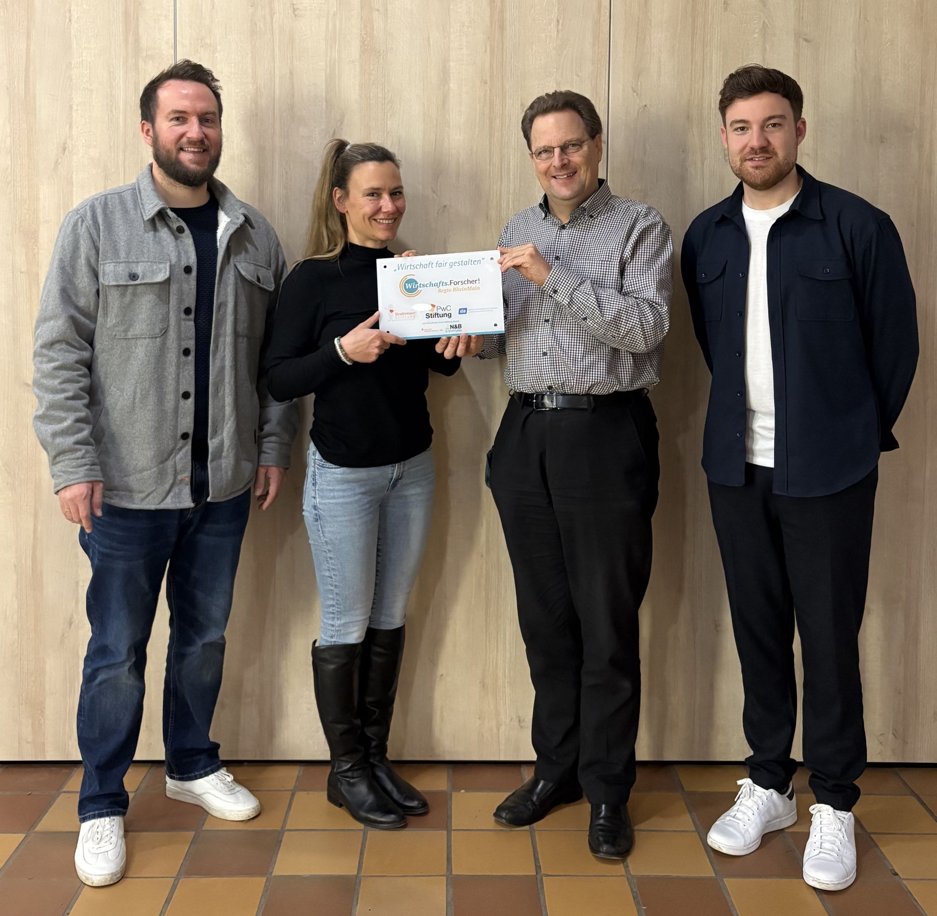 Alexander Hübner (Strahlemann, links) und Maximilian Porrmann (PwC-Stiftung, rechts) übergeben den HOLA-Lehrkräften Janina Endner und Stefan Prochnow die „WiFoLab-Plakette“ für ihr Engagement in der wirtschaftsethischen Bildung